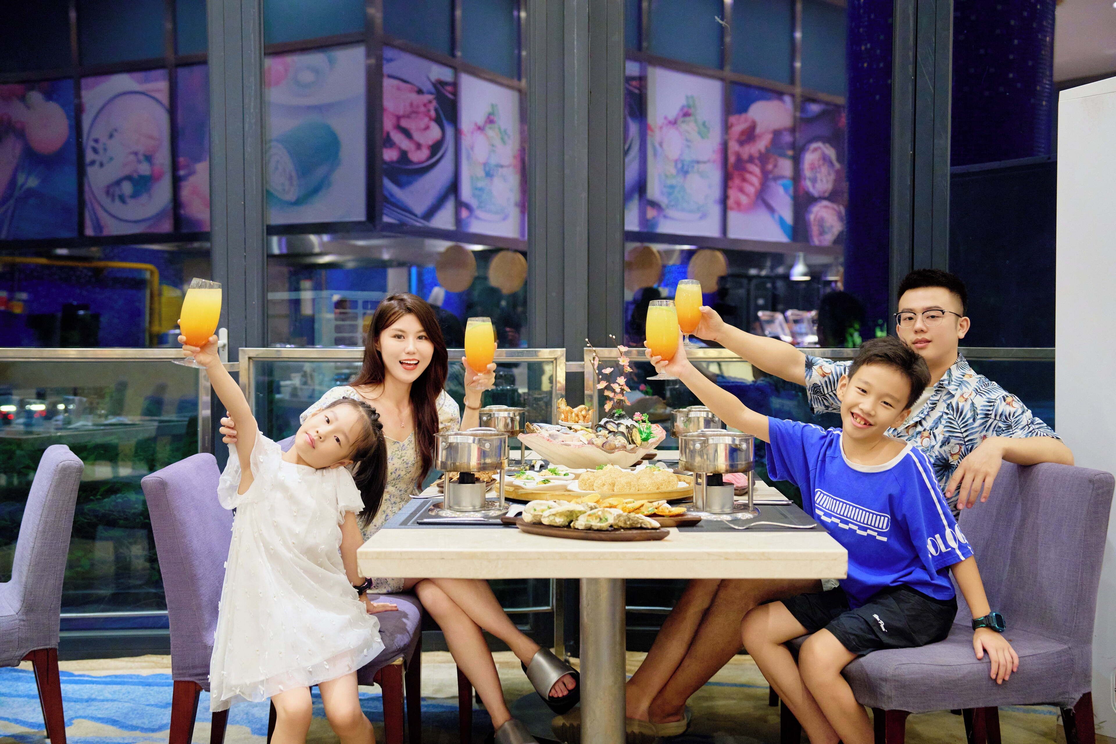 A group of people seated around a table with food and drinks, in a room with large windows and a city view.