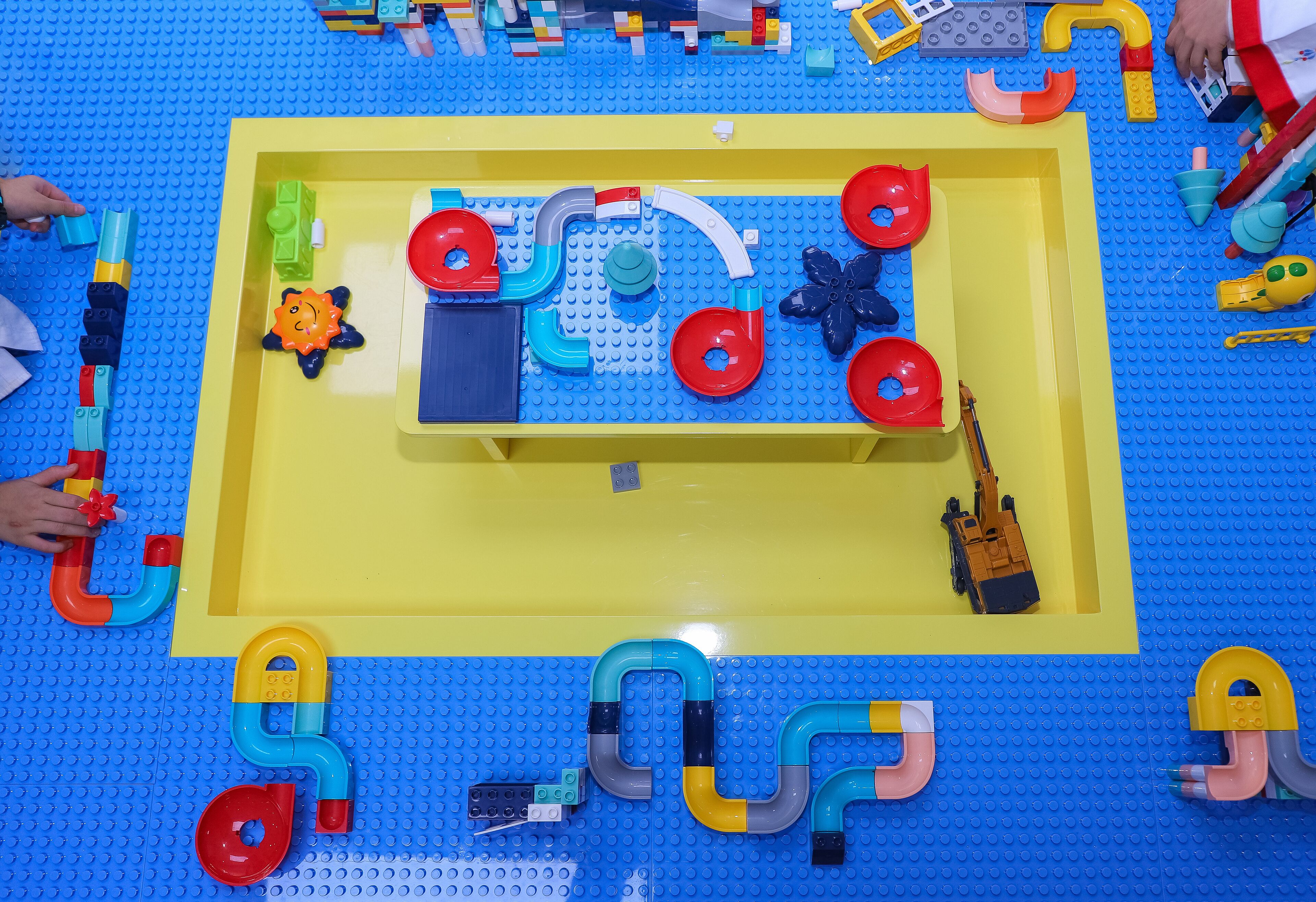 Un espace de jeux avec différents jouets et des jeux de construction, le tout sur un sol bleu et jaune.