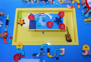 Un espace de jeux avec différents jouets et des jeux de construction, le tout sur un sol bleu et jaune.