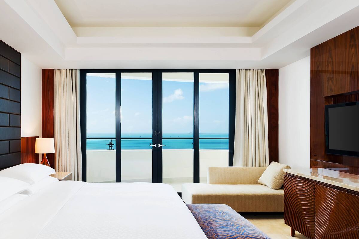 A hotel room with a bed, a sofa, a TV, and a view of the ocean.