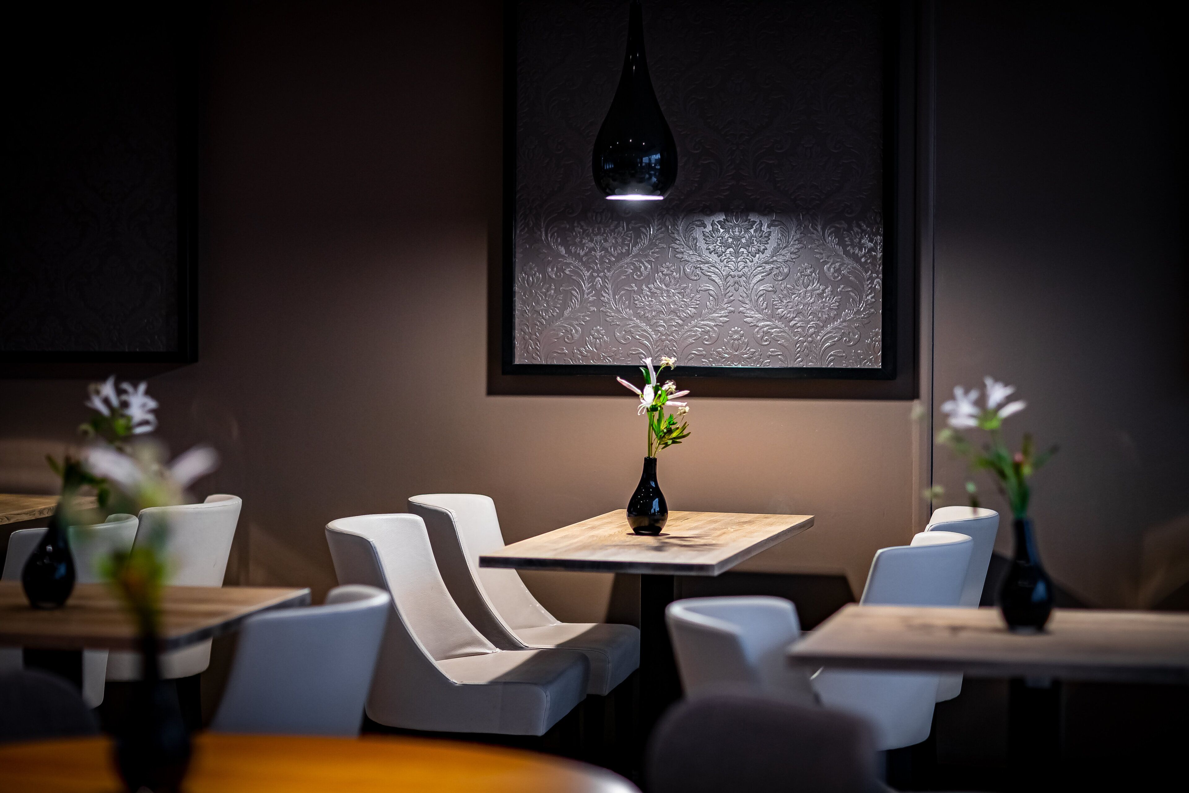 A modern interior with a minimalist design, featuring a table with a vase of flowers, white chairs, and a hanging light fixture.