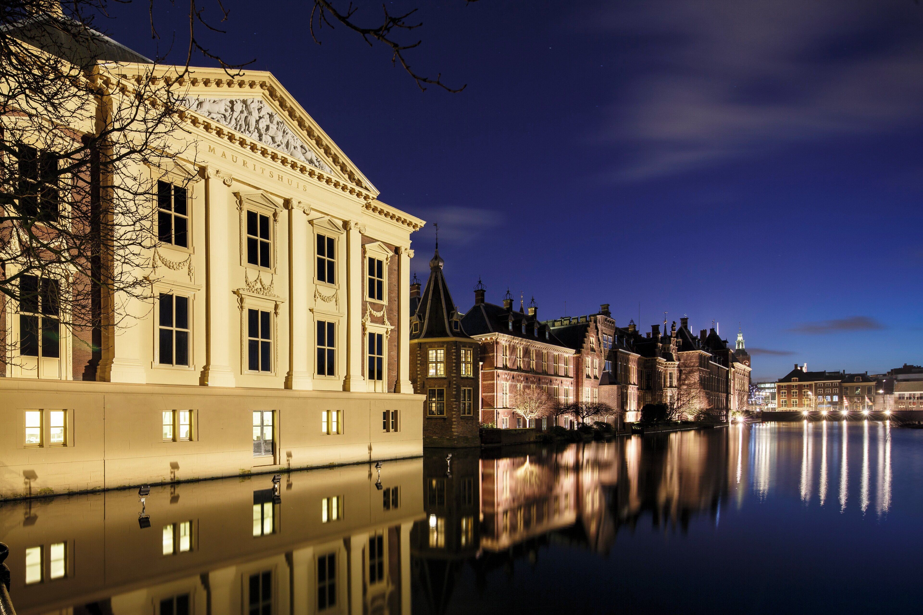A historic building with classical architecture, a reflection in the water, and a clear night sky.