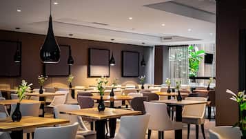 A modern restaurant interior with multiple tables and chairs, pendant lighting, and framed artwork on the walls.