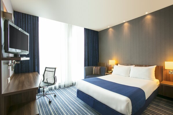 A hotel room with a bed, a desk with a chair, a television, and a window with curtains.