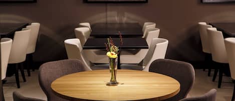 Un comedor con mesas redondas, sillas y un florero con flores.