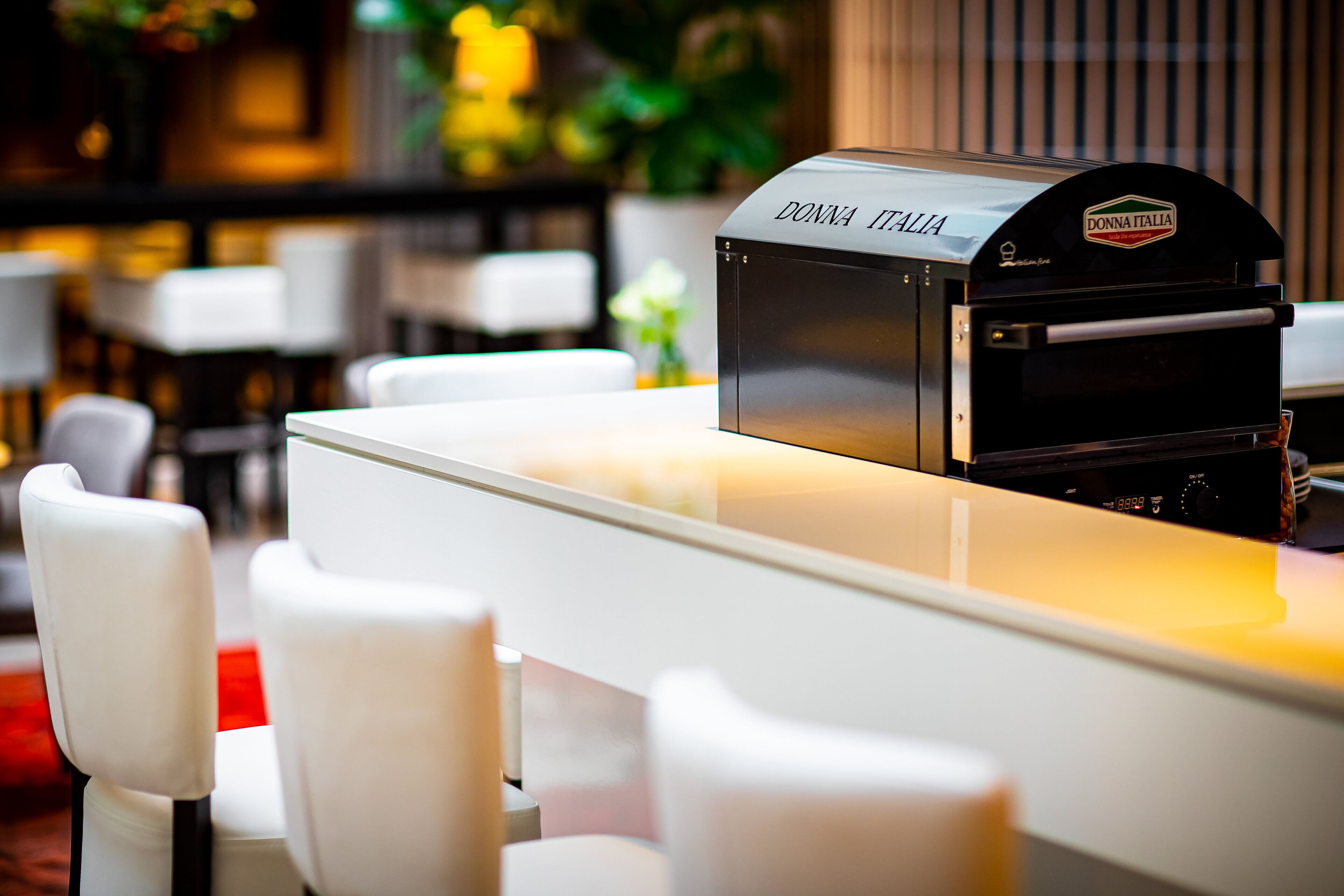 A modern bar area with a branded coffee machine, white bar stools, and a clean, contemporary design.