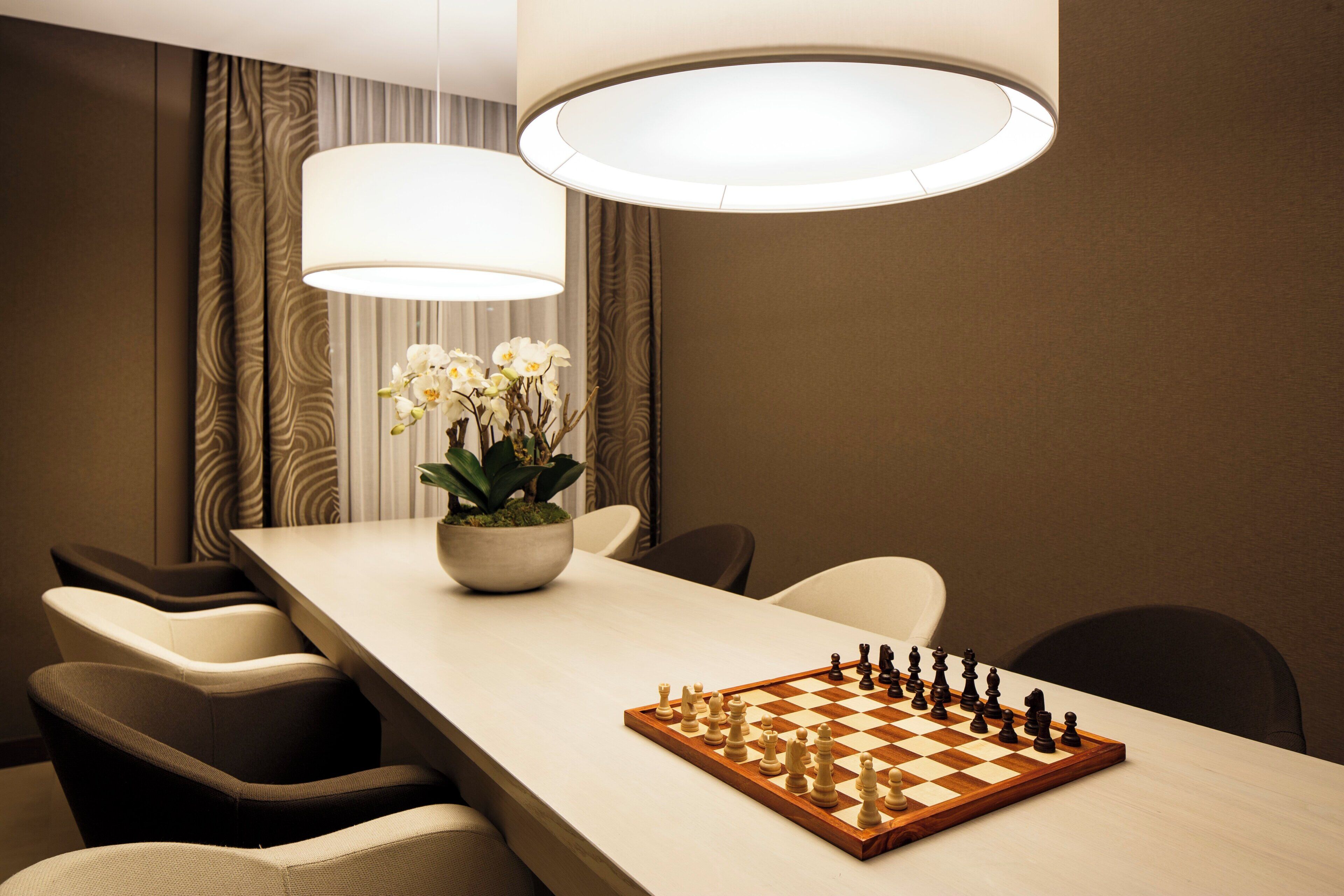 A hotel room with a long dining table, a chessboard, and a potted plant.