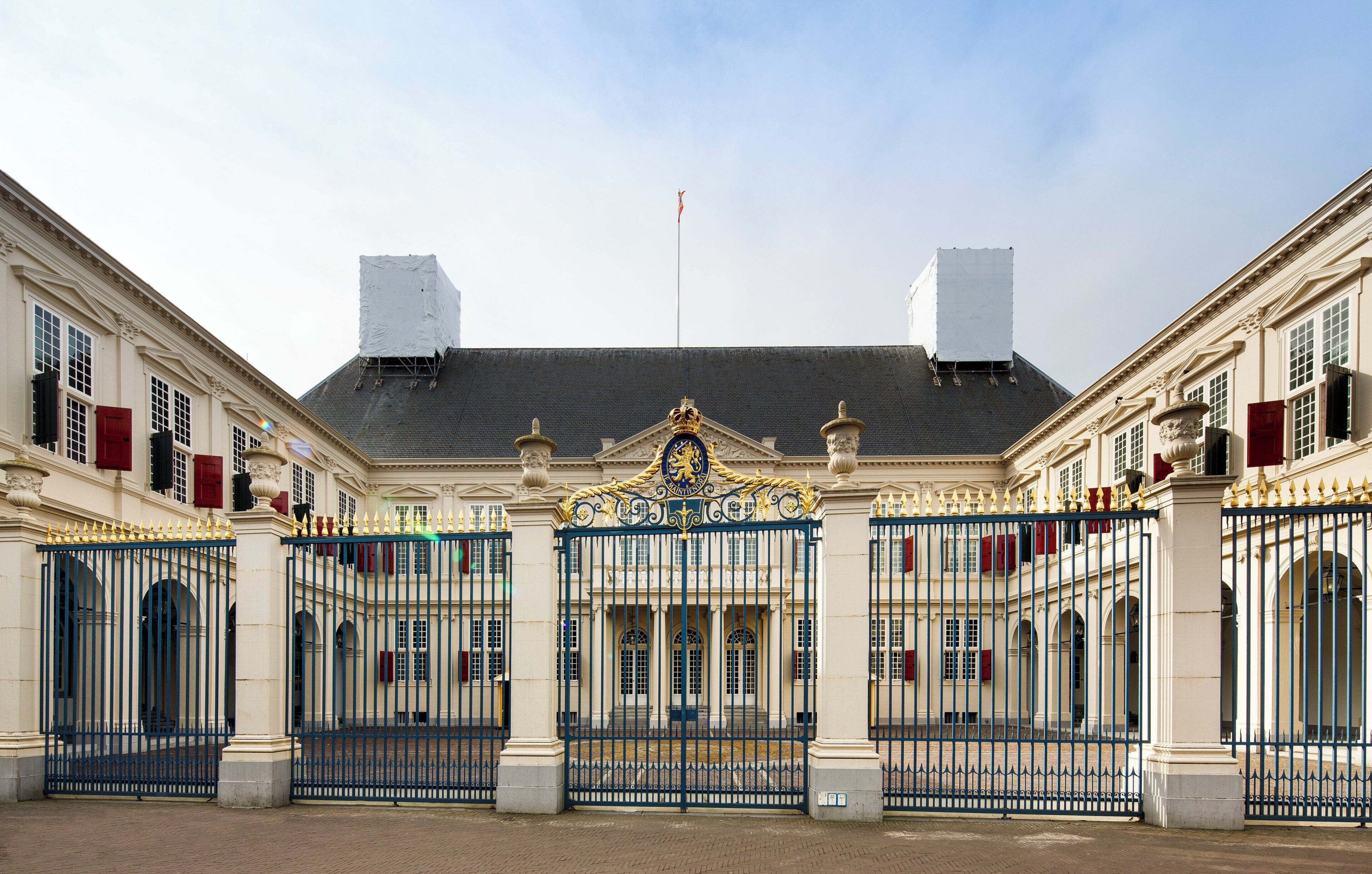 A grand entrance with a decorative gate, a flagpole, and symmetrical buildings with red shutters.