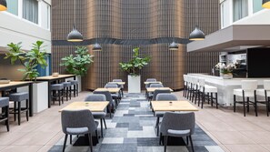 A modern restaurant with a central seating area, a bar on the right, and a vertical wooden panel wall.