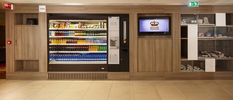 A vending machine stocked with beverages and snacks, a television displaying 'GOING OUT DUTCH', and a display of ceramics.