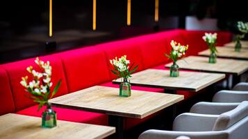 Filas de mesas con jarrones de flores, asientos rojos y sillas grises en un ambiente de restaurante.