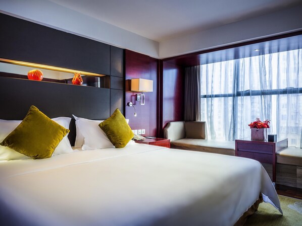 Une chambre d’hôtel avec un grand lit, une table de chevet, une chaise, une fenêtre avec des rideaux et une étagère murale agrémentée d’objets décoratifs.