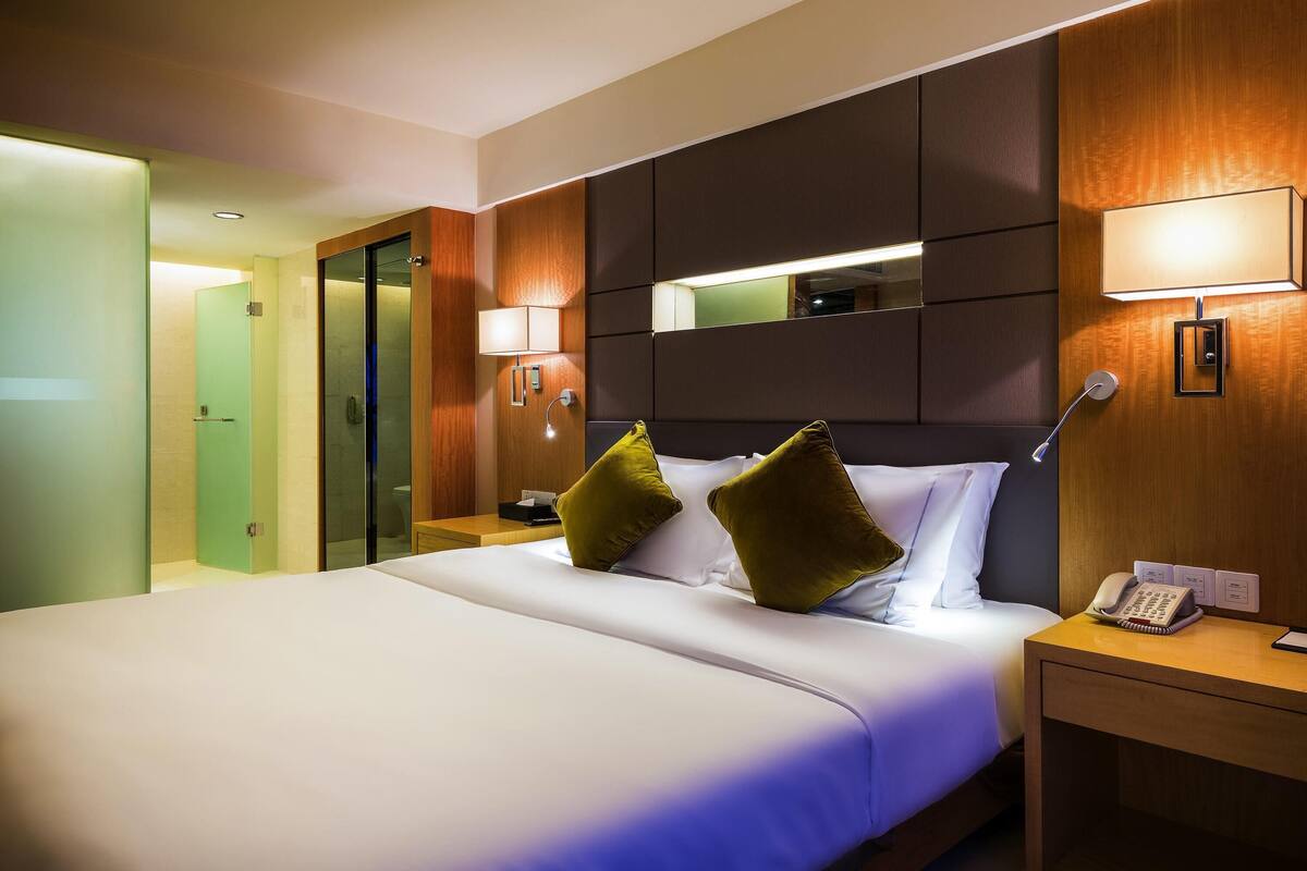 Ein Hotelzimmer mit einem Bett, Nachttischlampen, einem Nachttisch mit Telefon und einem Spiegel über dem Bett.