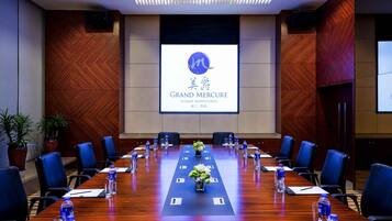 A conference room with a long table, chairs, water bottles, and a screen displaying 'GRAND MERCURY XIAMEN DOWNTOWN'.