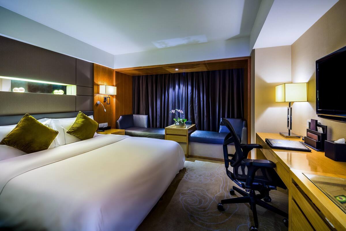 Ein Hotelzimmer mit Bett, Schreibtisch, Stuhl, Fernseher und einem Fenster mit Vorhängen.