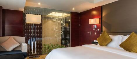Una habitación de hotel moderna con una cama grande, un sofá, un separador de vidrio y una lámpara espiral decorativa.