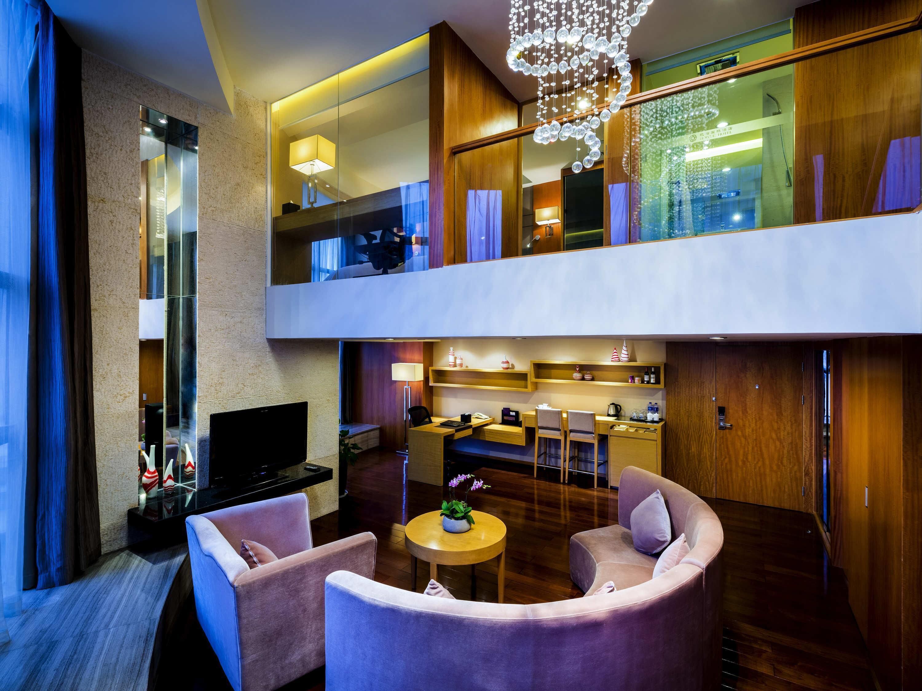 Una habitación de hotel moderna con una televisión de pantalla plana, un sofá, una zona de comedor y un balcón con vistas.