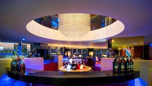 Ein moderner Barbereich mit einer kreisförmigen Sitzanordnung, einer zentralen Bartheke und einer großen Chandelier.