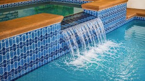 Una piscina con azulejos azules estampados y una cascada.