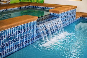 Une piscine avec des carreaux bleus à motifs et une cascade décorative.