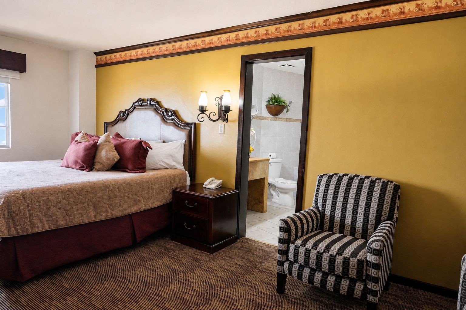 Una camera d'albergo con un letto, un comodino, una sedia e un bagno visibile attraverso una porta aperta.
