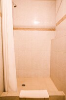 Un baño pequeño con azulejos, una banqueta y un cabezal de ducha.
