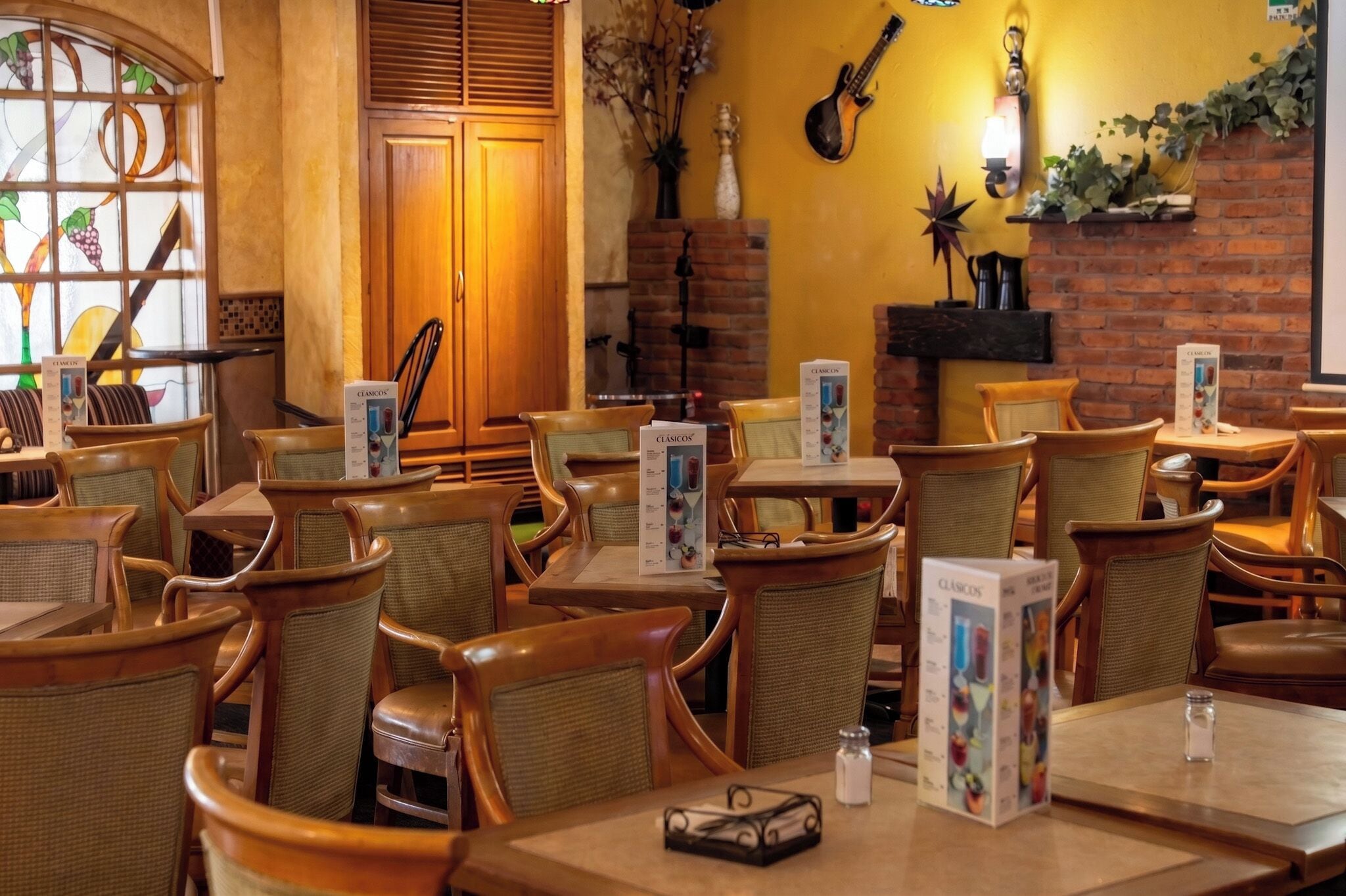 A restaurant with wooden tables and chairs, menu boards, a brick wall, and a guitar.
