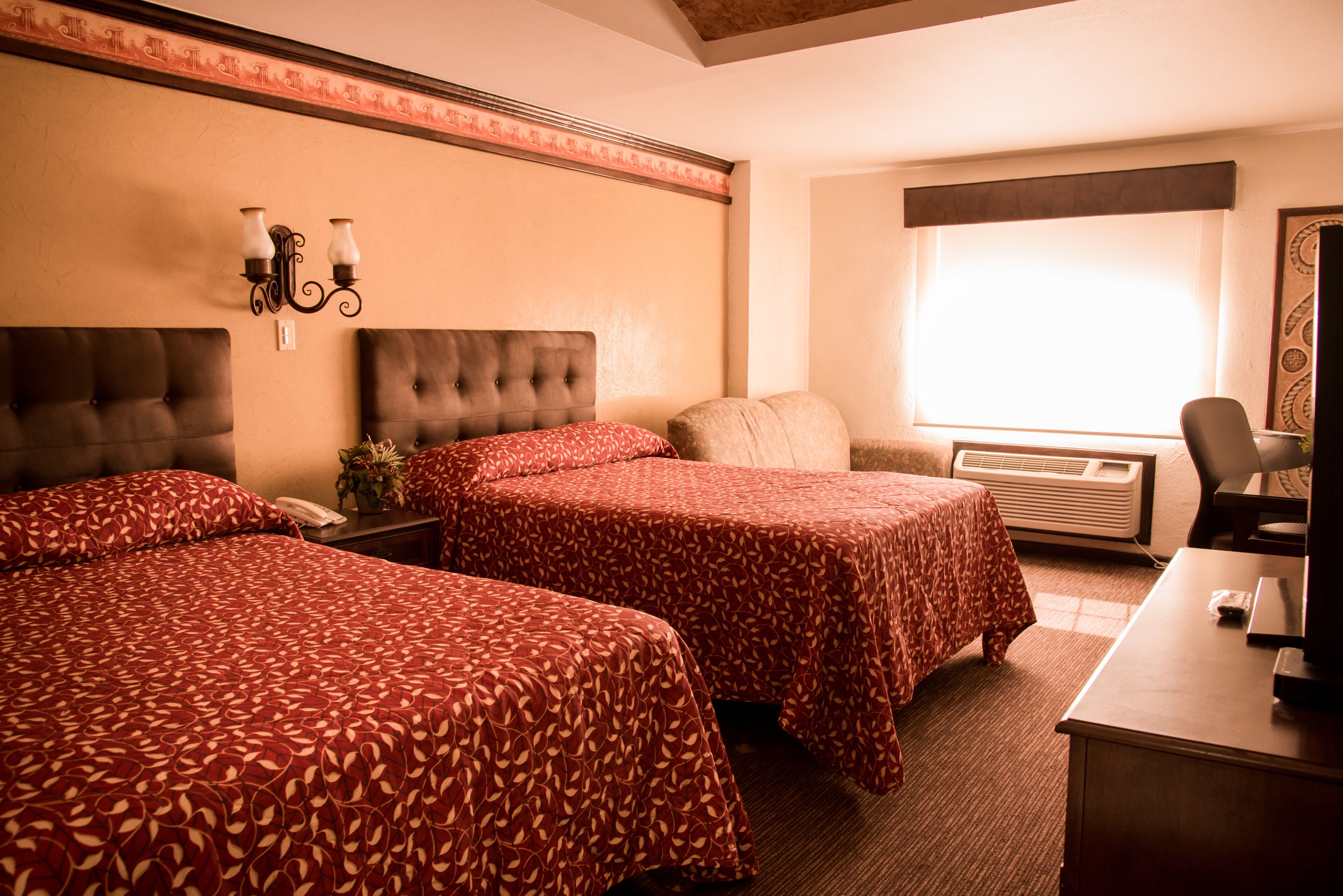 A hotel room with two beds, a desk, a chair, a telephone, and an air conditioning unit.