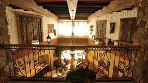 Un interior tradicional con vigas de madera a la vista, paredes de piedra y un balcón con barandillas de hierro forjado.