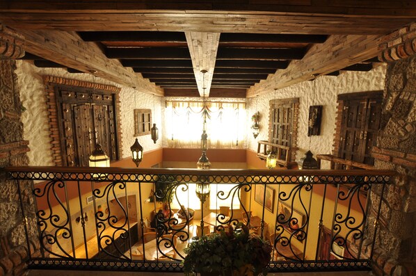 A traditional interior with exposed wooden beams, stone walls, and a balcony with wrought iron railings.
