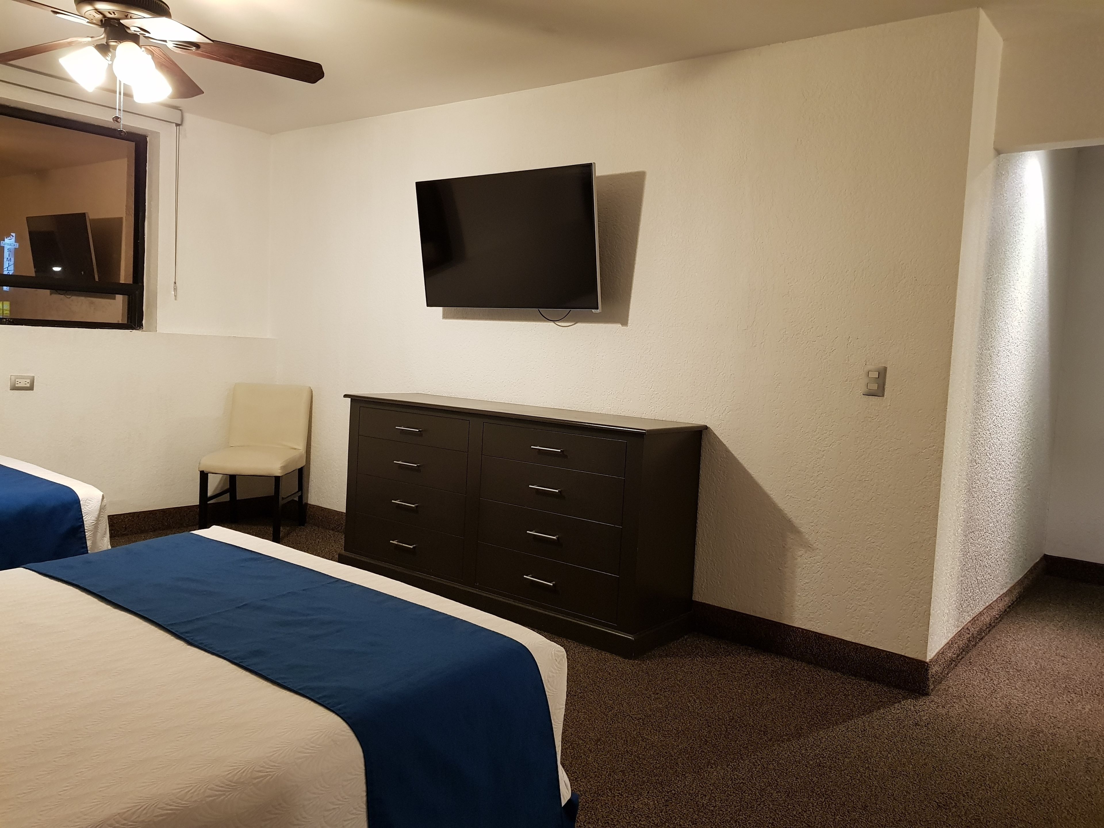 Habitación de hotel con dos camas, un aparador, un televisor y un ventilador de techo.