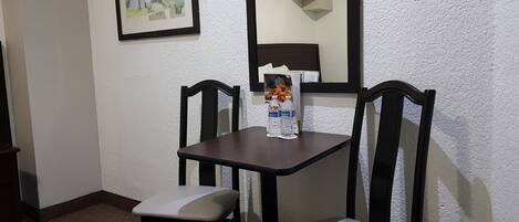 Un pequeño comedor con una mesa y dos sillas, un cuadro en la pared y una botella de agua sobre la mesa.