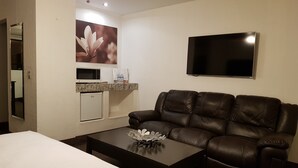 Una habitación de hotel con una cama, un sofá de cuero, una kitchenette pequeña, un televisor de pantalla plana y un florero decorativo.