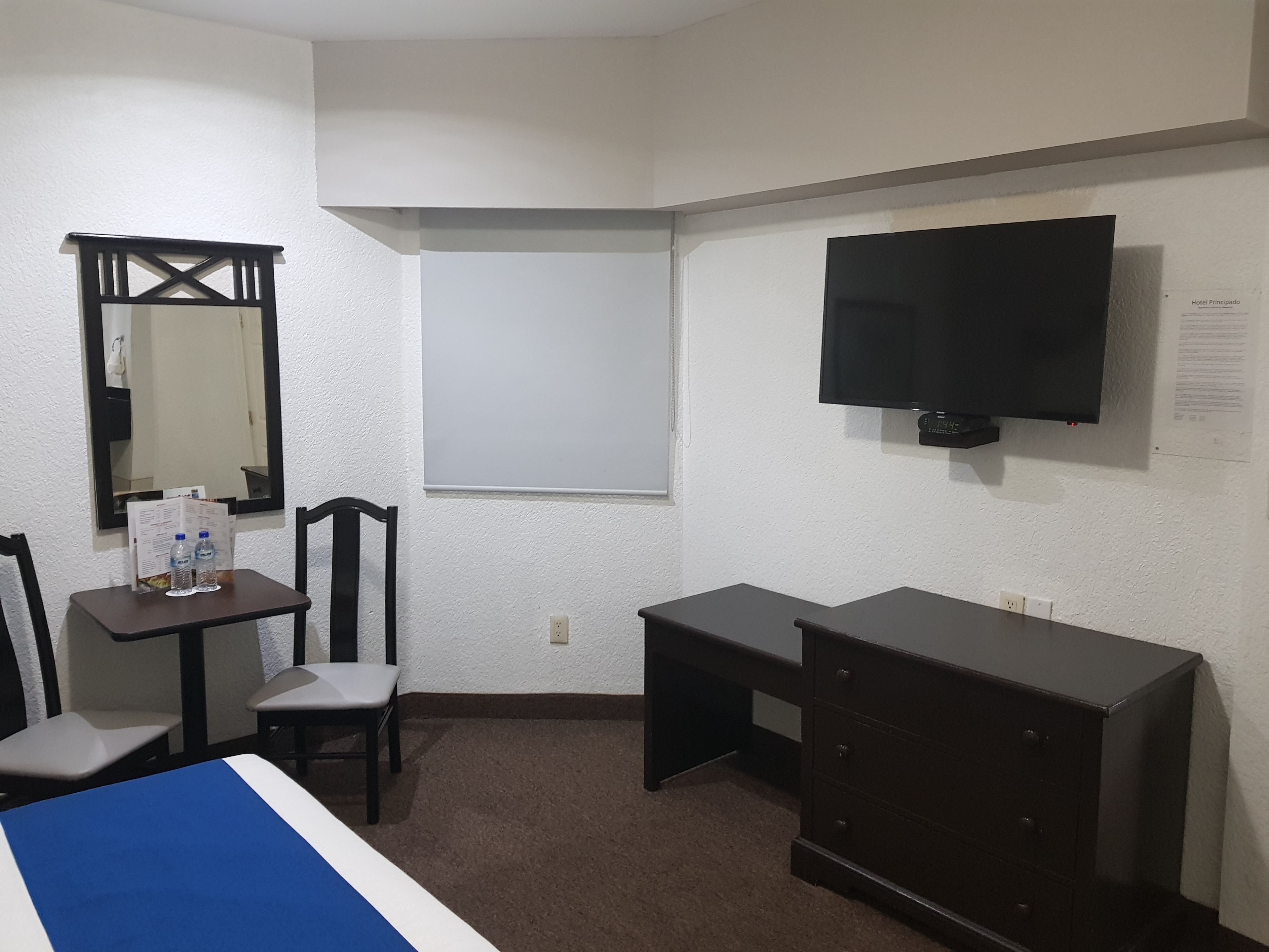 A hotel room with a bed, a desk, a dresser, a TV, a mirror, and a chair.