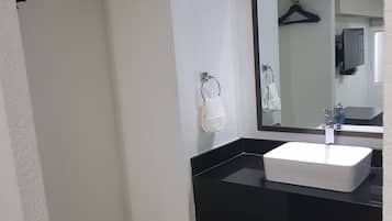 Un baño con lavamanos blanco, encimera negra y un espejo encima.