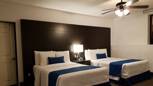 Habitación de hotel con dos camas, cabecera oscura, paredes blancas y ventilador de techo.