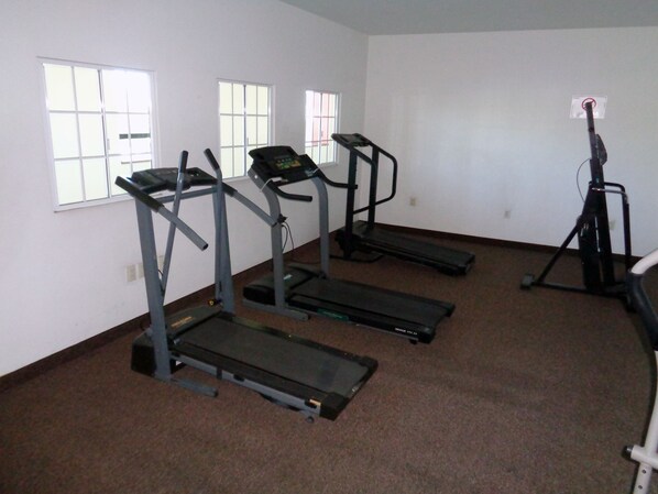 A room with three treadmills, a stationary bike, and a wall-mounted exercise machine.