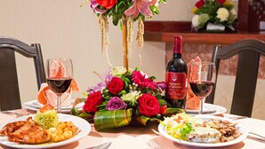 Una mesa de comedor dispuesta con platos de comida, copas de vino y un centro de mesa con flores.