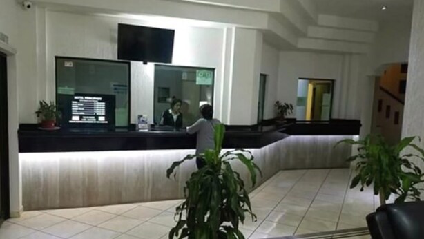 Zona de recepción de un hotel con un mostrador, un televisor de pantalla plana y un panel de visualización digital.