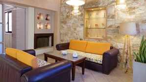 A cozy living room with a stone wall, a fireplace, a sofa, and a coffee table. - Elea apartments (Chania)