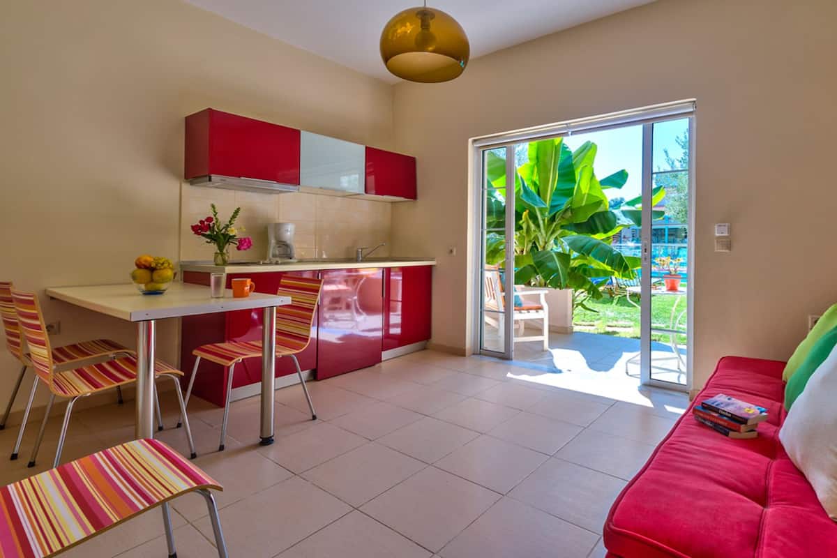 A compact living space with a kitchenette, a dining area, and a seating area with a red sofa and striped chairs.