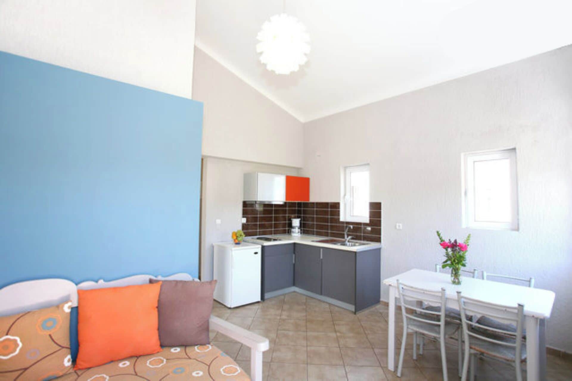 A compact living space with a kitchenette, a dining area, and a sofa with patterned cushions.