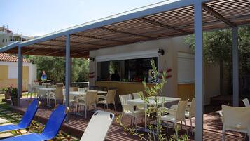 Un patio al aire libre con mesas y sillas, una zona de bar y un área de estar cubierta.