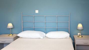 A bed with a white mattress and two white pillows, flanked by two bedside tables with lamps, against a blue wall.
