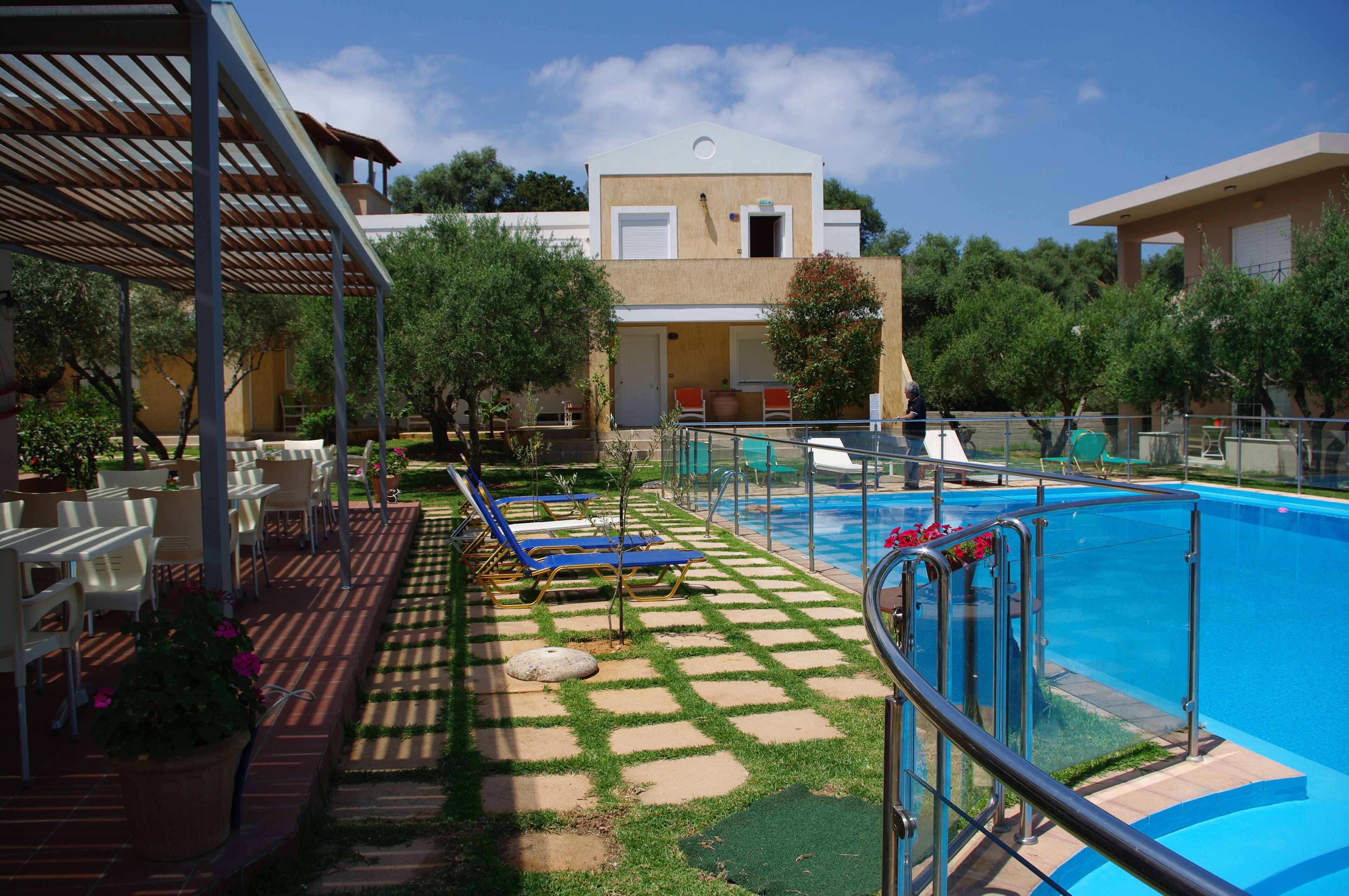 Zona junto a la piscina con vista despejada, sillas de descanso y un área de estar cubierta.