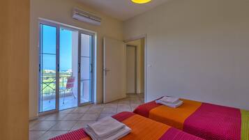 Quarto de hotel com duas camas, uma varanda com cadeira e vista para o mar.