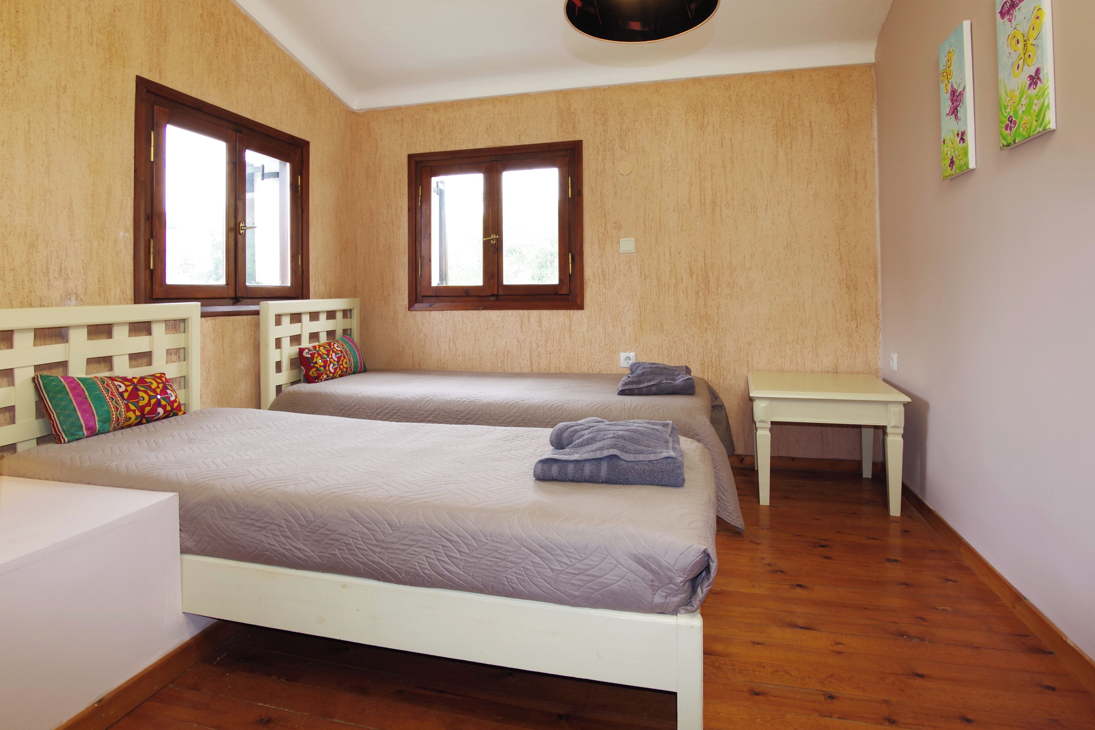 Una habitación con dos camas, una mesita y dos ventanas.