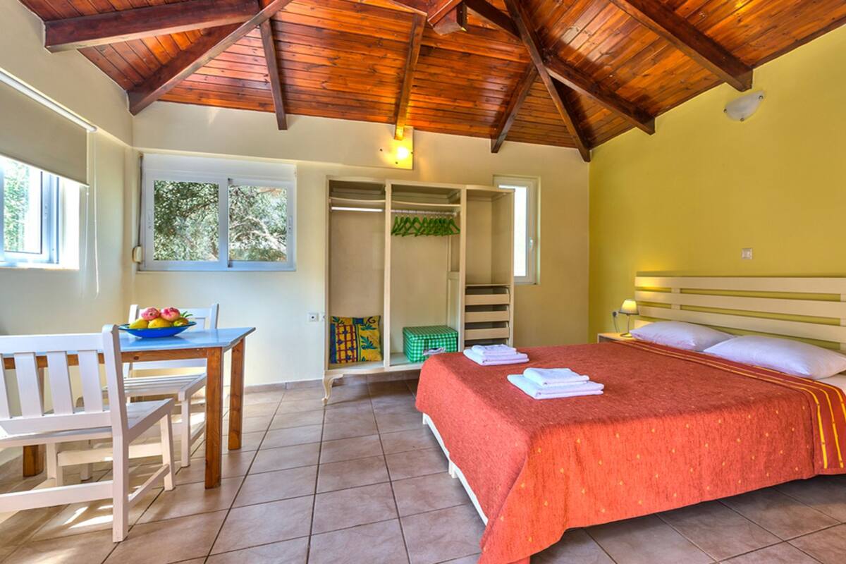 A bedroom with a bed, bedside table, and a desk with chairs. There is a window and a door leading to a bathroom.