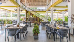 A spacious indoor dining area with multiple tables and chairs, a central staircase, and a television screen. - Cambodian Country Club (Phnom Penh)