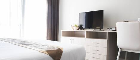 Une chambre d’hôtel avec un lit, un bureau, une télévision et une fenêtre avec des rideaux.
